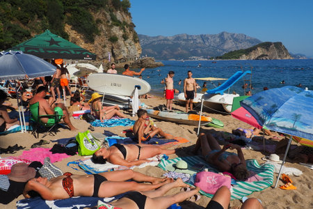 Budva, Montenegro, Mogren beach. August 15 2022 Sand and pebble beach near high cliffs. Beach umbrellas, cafes, deck chairs. People relax, swim, enjoy and sunbathe. Tourism business in the Balkans.のeditorial素材