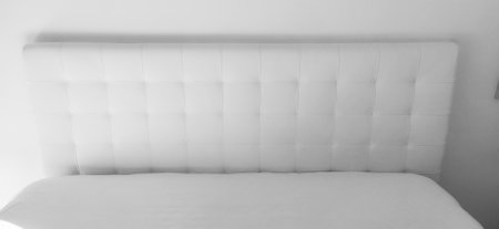 Soft headboard. Upholstery for furniture made of genuine or artificial leather and quilted fabric. Soft headboard against a light wall. Black and white monochrome photoの写真素材