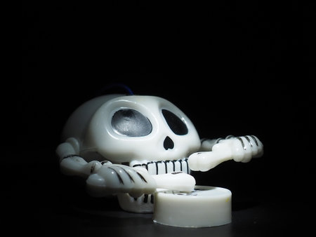 Skull with drumsticks and drum. Terrible clockwork toy. The skeleton is made of the skull, bones, hands and fingers. Black background. Halloween and horror theme. White skull with black eye socketsの写真素材