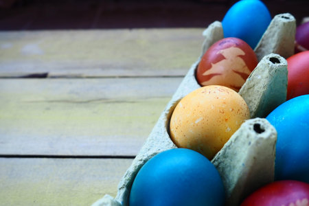 Multi-colored eggs painted with gouache and onion peel in a cardboard box on a wooden table...