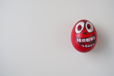 Easter egg painted red, white and black with a cheerful toothy face. Boiled chicken dyed egg with red shell. White background. Big eyes, white teeth on the fun face. Copy spaceの写真素材