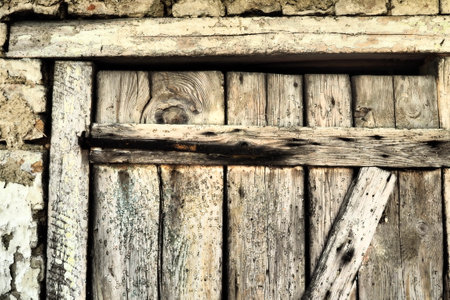 Locked old wooden door of a rural barn. Texture of a wooden board and rusty iron staples. Closed door of an ancient building. Abandoned, forgotten, crumbling building.の写真素材