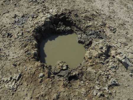 Crater with gray volcanic healing clay. A hole with a prominent amorphous mass from the depths of the earth. Mud and gas eruption. Temryuk, Russia. Cracked soil surface. Texture of a mudflow cracksの写真素材