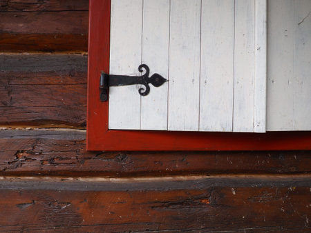 Ethno-folk wooden shutters on a window with a wooden frame, painted red and white. Metal loop...