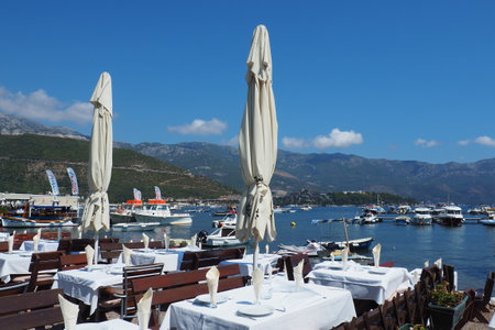 Budva Montenegro 8.15.22 Adriatic sea Mediterranean riviera. Tourism business. Yachts, boats and pleasure craft. Restaurant by the sea, first line. Tables, chairs, sun umbrellas and white tablecloths.のeditorial素材