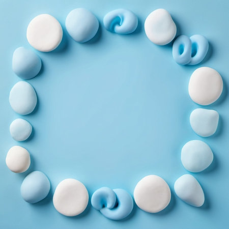 A blue background is surrounded by a frame of white and blue plasticine stones, arranged in a circular shape. AI generated. Copy space in the middle of the image.の素材