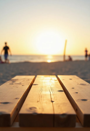 A wooden table stands in the foreground, warm sunlight casting a golden hue, as beachgoers stroll along the sandy shore, enjoying the serene ocean view during sunset.の素材