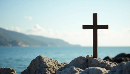 A wooden cross stands majestically on weathered rocks near the sea, with gentle waves lapping at the shore.の素材