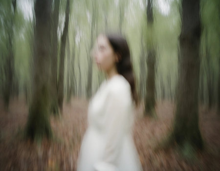 In a dense, fog-filled forest, a spectral woman wearing a flowing white dress stands among towering trees. The eerie atmosphere captures the sense of an otherworldly presence at dusk.の素材