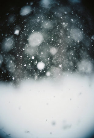 Snowflakes drift down slowly, covering the ground in a thick layer of white. The scene is blurred, showing the chill of winter.の素材