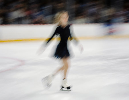 A young skater glides across an ice rink with blurred surroundings. The scene captures winter excitement, with an audience enjoying the holiday spirit.の素材