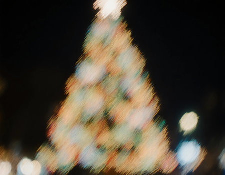 A Christmas tree is illuminated with bright lights in a festive setting. The scene captures the joy of the holiday season during the night, evoking a cheerful spirit.の素材
