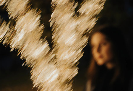 A woman stands near a Christmas tree with bright lights creating a bokeh effect. The setting shows festive decorations for the holiday season.の素材