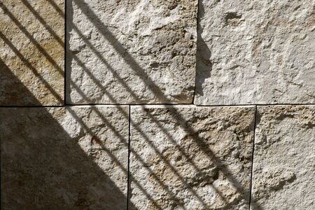 A railing shadow falls diagonally on a textured granite block wall in the afternoon sun.の写真素材