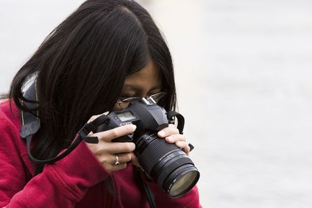 A young Asian girl looks down through the view finder of her digital camera.の写真素材
