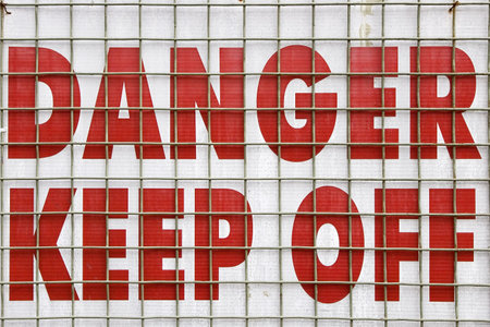 Danger Keep Off in bold red letters on a sign behind a wire fence.