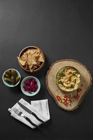 Humus. Halva with tahini and organic chickpeas. Whole wheat lavash chips, pickled cucumbers with red sauerkraut served together. White napkin and serving on black background. Still life food.の写真素材
