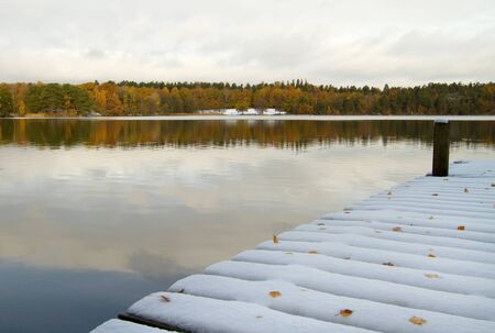 Snow covered jetty at calm lake in early winter.の写真素材