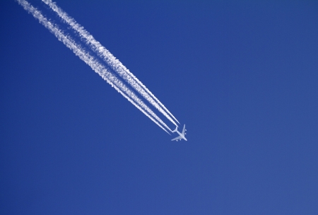 Airplane with condensation trails on blue sky の写真素材