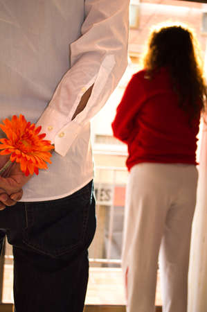 Man hiding flower and woman looking out the windowの写真素材