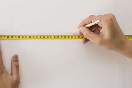 Closeup of a measuring tape and  pencil marking with a white wallの写真素材