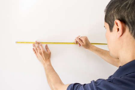 Closeup of people pointing at a measuring tape on the wall and marking with pencilの写真素材