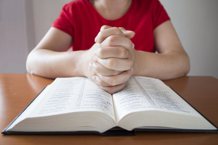 women hands folded in prayer over a holy bible