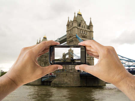 tourist holds up camera mobile at tower bridge in london englandの写真素材