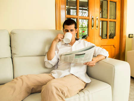 Man drinking coffee and reading newspaper on the sofaの写真素材