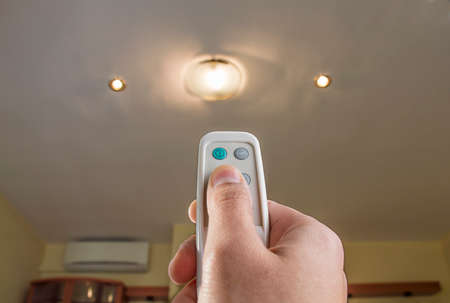 hand pressing a remote control controlling an lightの写真素材