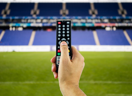 Hand holding television remote for watching sports in 3D