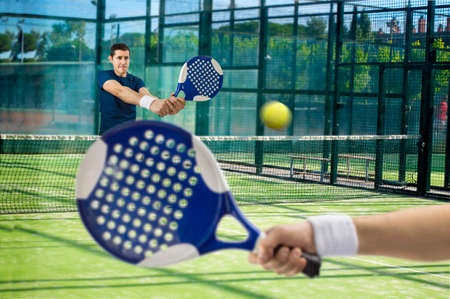 men playing paddle tennis standing and swatting the ball on courtの写真素材