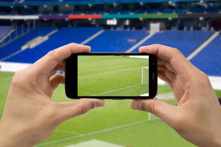 hand the tourist takes a picture with his mobile of the football stadiumの写真素材