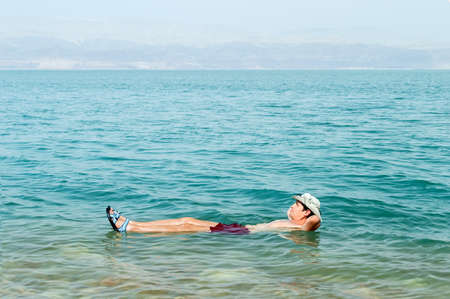 Man floating in a glassy water of dead sea with outstretched arms の写真素材