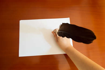 Woman s hand with feather pen writing down notes with copy spaceの写真素材