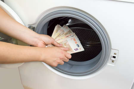 hand putting money into the laundry machine in  concept crime of Money Laundryの写真素材