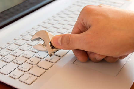 Hand holding spanner on a  laptop keyboard in  repair conceptの写真素材