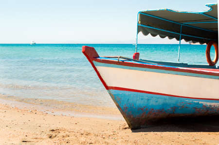 red sea with a wooden old and broken white blue boat on beach on warm sunset on jordanの写真素材