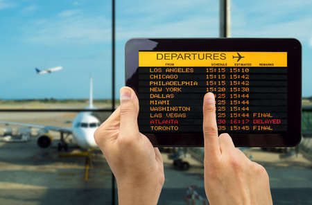 Hand holding tablet with connect wifi on the airport and see departures boardの写真素材