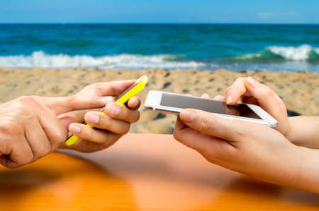 two people with the phone and connected to social networks in a beachside barの写真素材