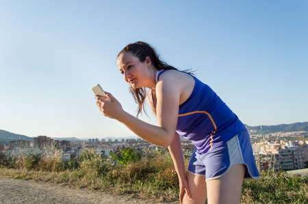 Fit runner woman taking a break while jogging. Young brunette female runner resting while listening to music with a mp3 player and earphones.の写真素材