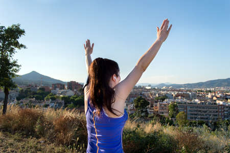 Happy cheering woman in park of the city enjoying view and sun. Fitness female joyful and excited after running.の写真素材