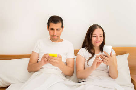 happy couple using social networking with their phones in the bedの写真素材