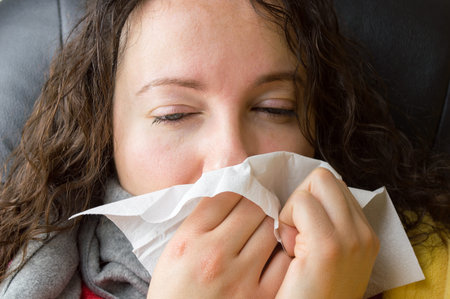 closeup of a sick woman sneezing with a tissue in herhand