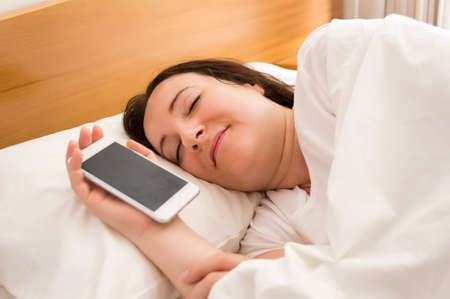 woman sleeping peacefully in bed with a phone in her handの写真素材