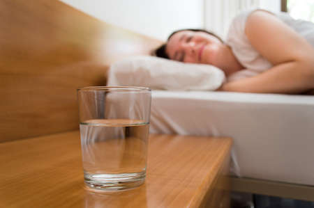 woman lying on bed with glass of mineral water on the nightstandの写真素材
