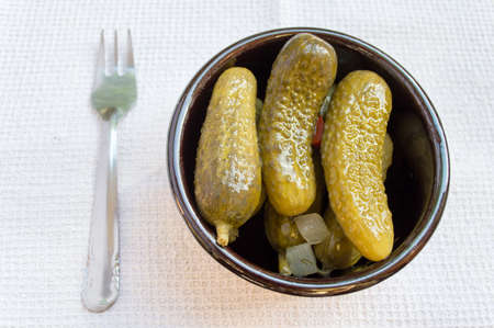 pickled cucumbers on a bowl with a fork over the tableの写真素材