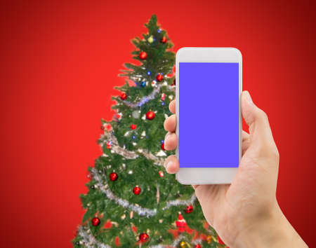 hand showing a smartphone with a Christmas tree backgroundの写真素材