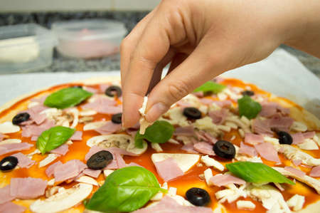 closeup of hand of woman putting mozzarella on the raw pizza  at the counter kitchenの写真素材