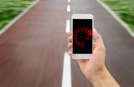 hand holding the smartphone with tachometer speed in the screen over the road in backgroundの写真素材